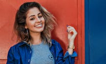 A woman in a denim jacket smiling brightly against a vibrant red and blue background.